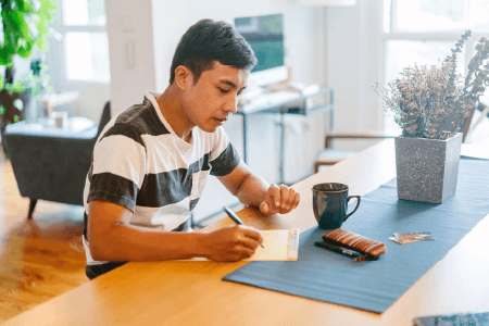 A person taking notes at a table with their coffee