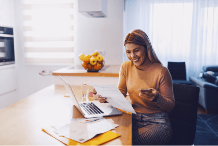 A woman smiling while at a table with a cellphone and laptop