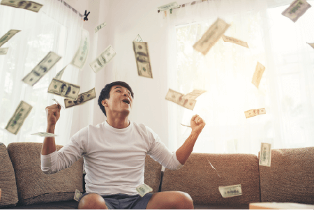 A man sitting on a couch and cheeering while cash rains down around him