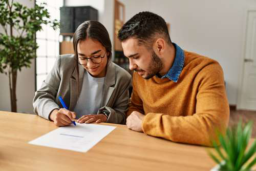 A man and woman sit together at a table, signing paperwork as co-signers for a title loan.